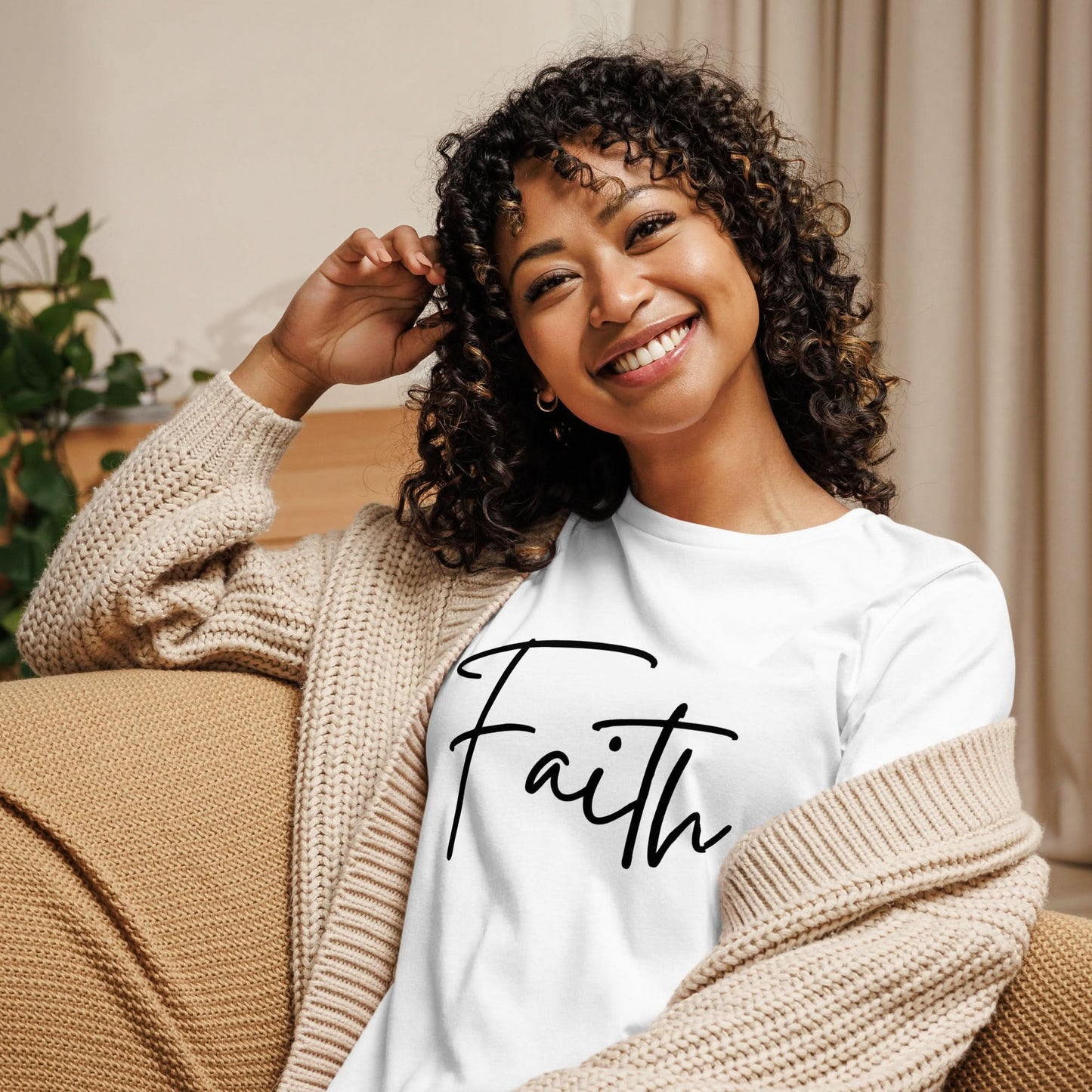 Smiling woman wearing Faith tee in black cursive lettering, styled in casual home setting with cozy cardigan.