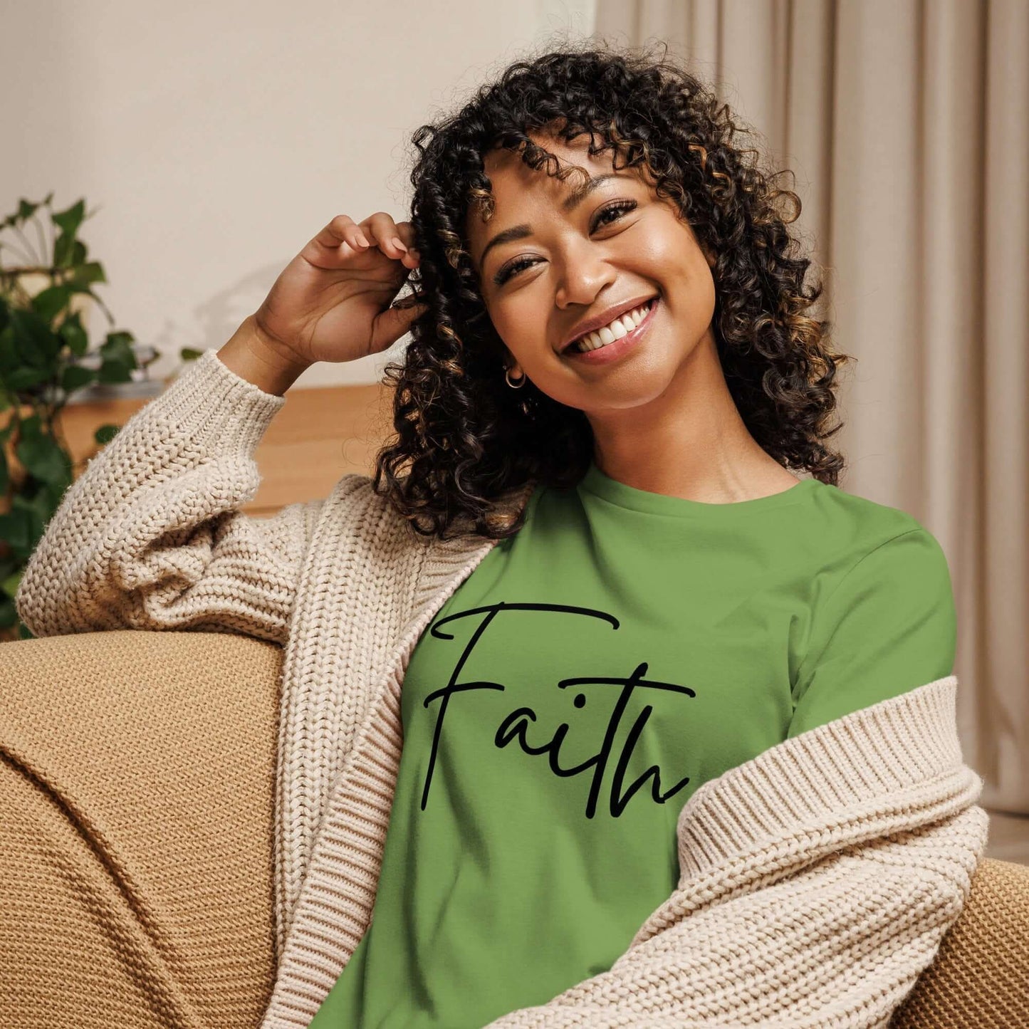 Woman wearing a green Faith tee with black cursive lettering, smiling on a cozy couch.