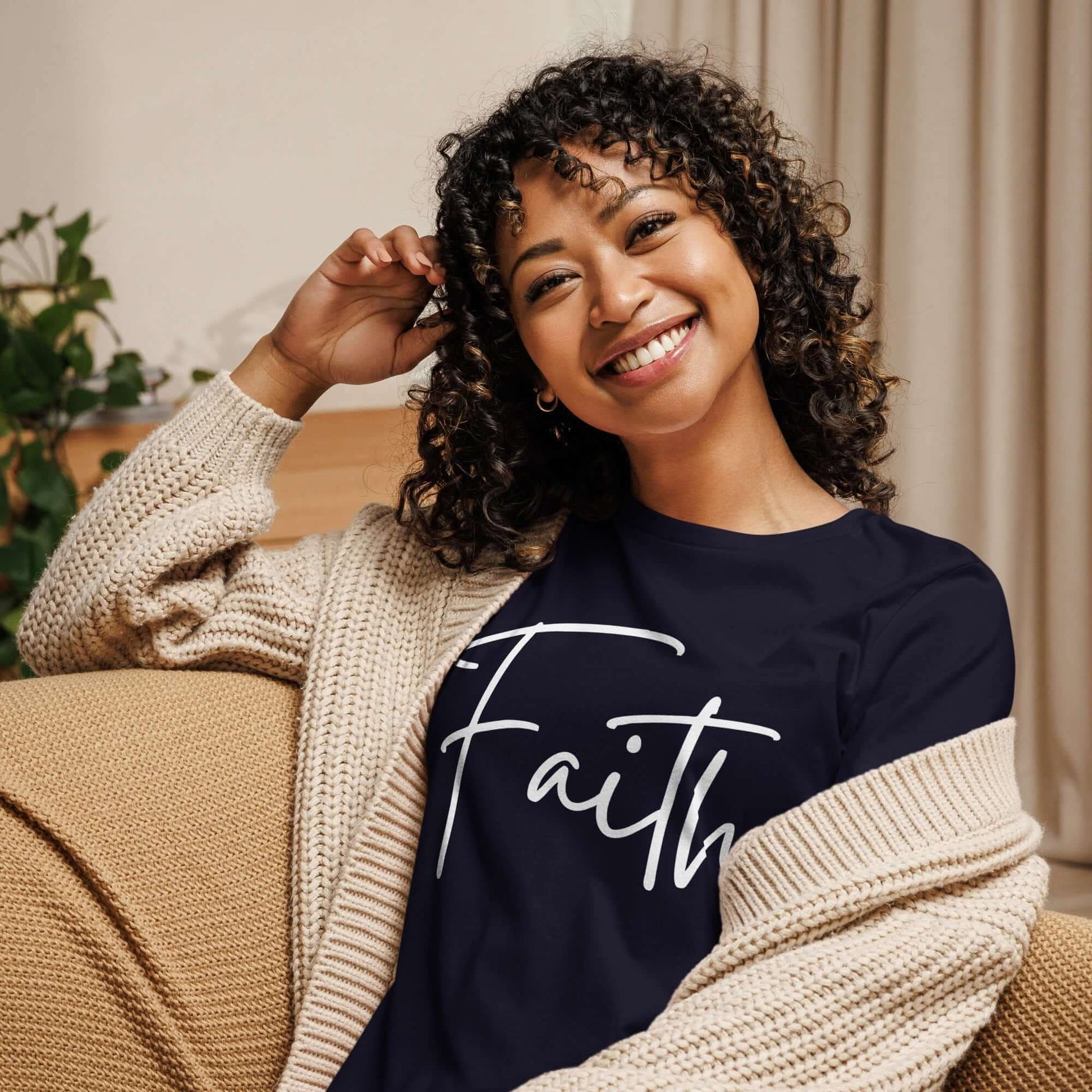 Smiling woman wearing a Faith tee in cursive lettering, seated comfortably on a couch.