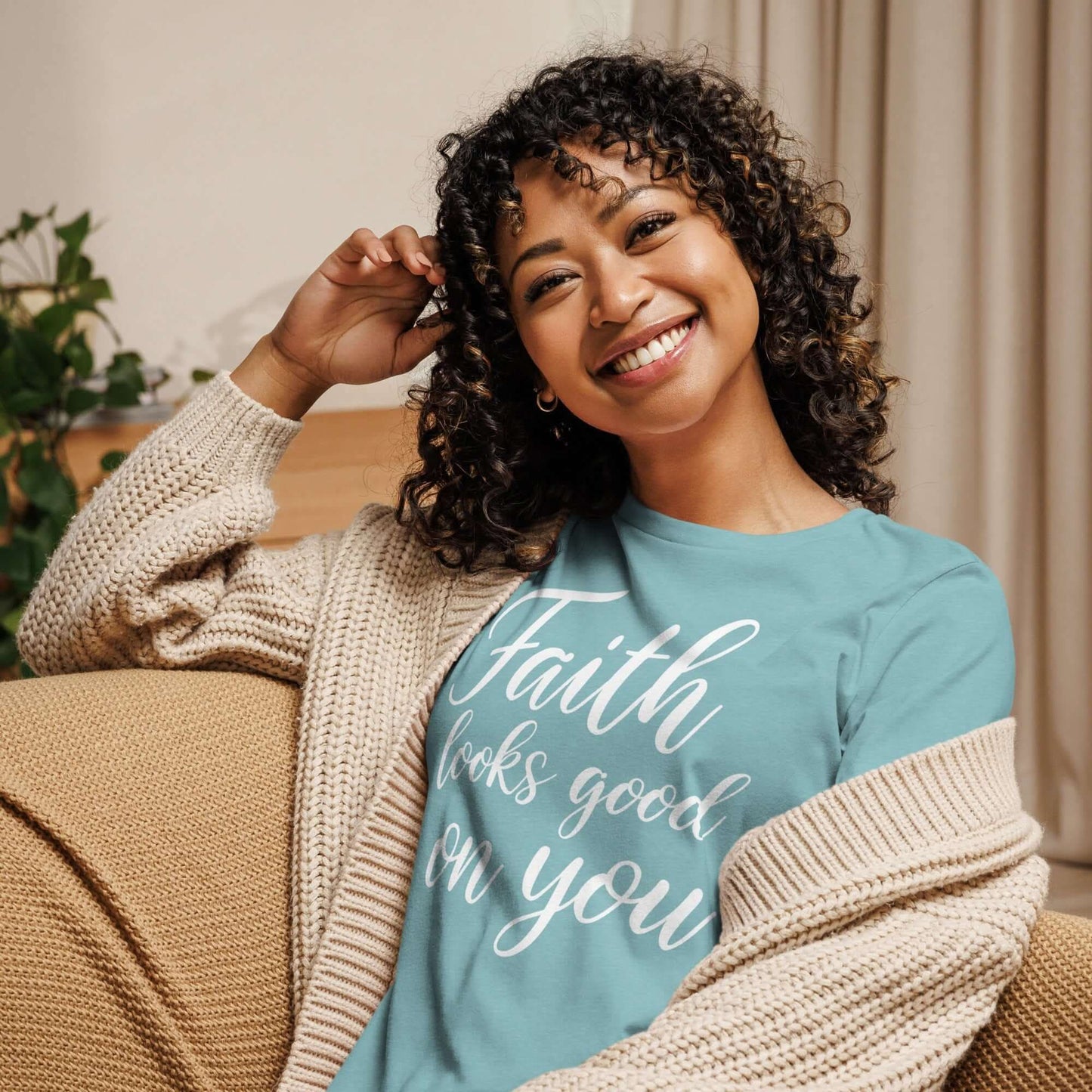 Smiling woman wearing Faith Looks Good on You Tee in light teal, styled with a cozy cardigan.